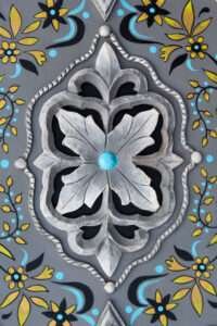 Ornate metalwork design with a central silver flower, accented by a blue dot. Surrounded by yellow and blue floral patterns on a gray background.