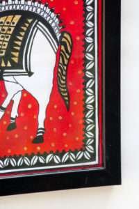 Framed artwork of a horse against a red background, adorned with geometric patterns and gold accents, conveys a traditional and vibrant feel.