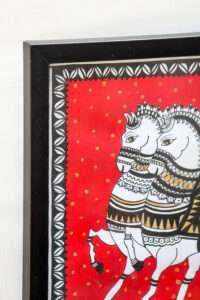 A framed painting of two stylized white horses with intricate black and gold patterns, set against a vibrant red background with golden dots.