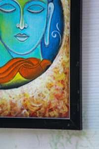 Close-up of a framed painting depicting a serene teal-faced buddha with closed eyes. Abstract patterns in orange and gold surround the face. Peaceful tone.