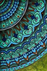 Intricate mandala with teal, blue, and green patterns featuring heart shapes, dots, and wavy lines. Conveys a feeling of harmony and complexity.