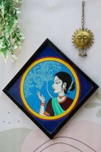 A beautiful women painting with a women in a saree with intricate jewelry, set against a blue backdrop with a stylized tree. A serene and elegant tone.