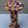 A cylindrical small round coffee table with a vibrant geometric pattern: orange base adorned with red, blue, and white shapes. It conveys a bold, artistic tone.