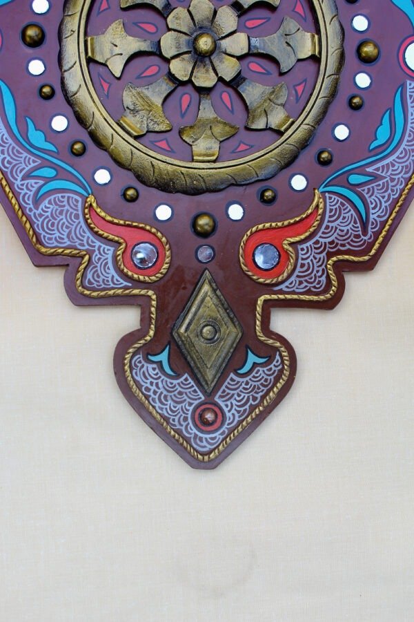 An ornate decoration features a central bronze flower surrounded by a circular pattern with red, blue, and white accents, set against a brown background.