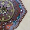 Intricate decorative wooden panel with floral and geometric patterns, featuring gold, red, black, and blue accents on a beige background. Ornate and elegant.