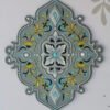 Ornate gray wall decoration with a central floral motif, surrounded by intricate yellow and blue designs. Elegant, symmetrical, and decorative.
