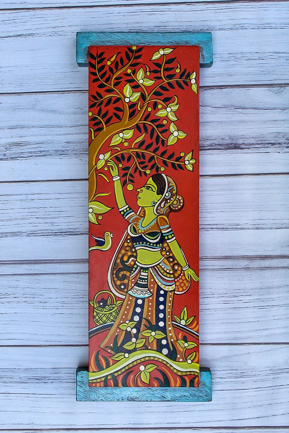 A vibrant wall hanging showcases a woman in traditional attire reaching for a tree branch with blossoms. A bird is nearby, all set against a rich red backdrop.